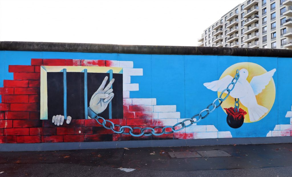 Mural of a person's hand from behind bars in a brick wall chained to a dove and a red flower.