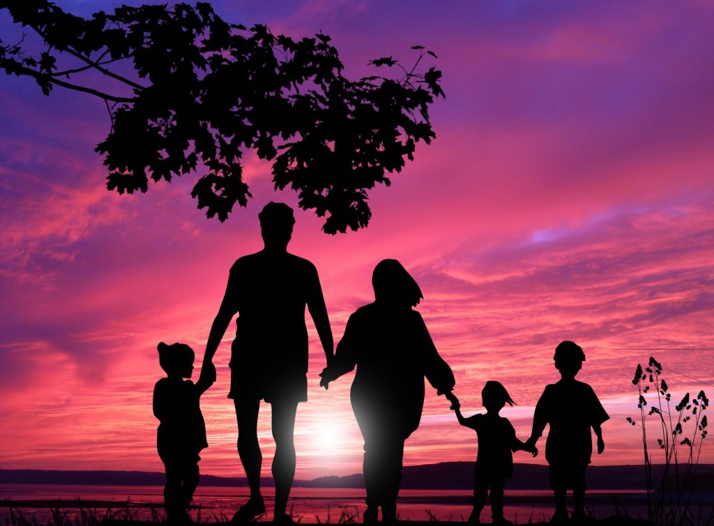 Silhouette of a family walking off towards a lake at sunset or sunrise, pink sky and trees.