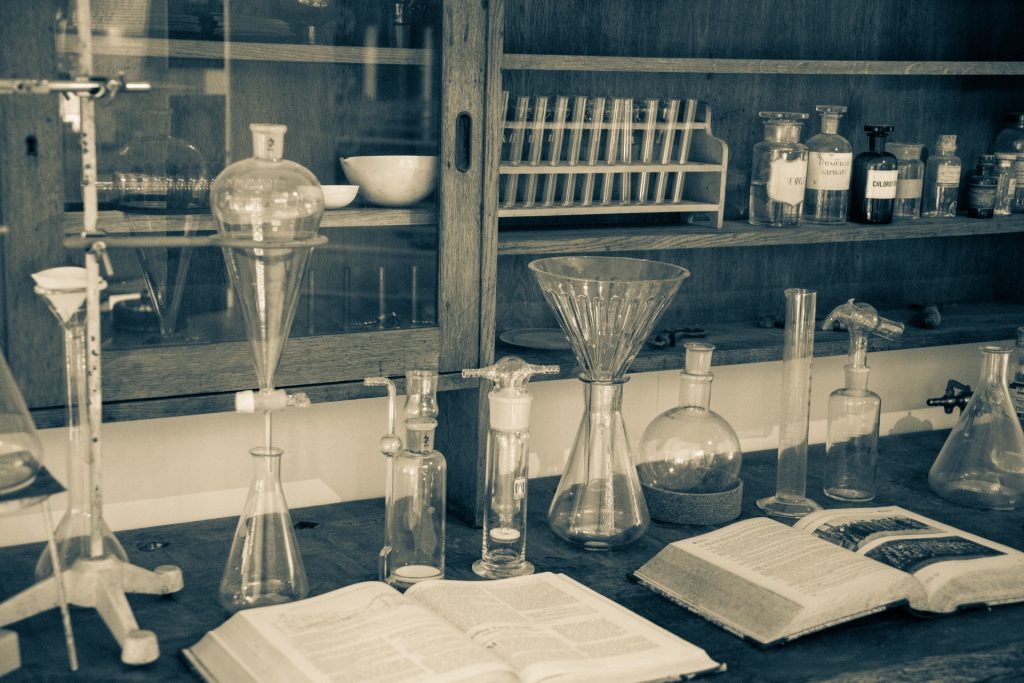 Old fashioned sepia toned photograph of a laboratory. Beakers, bottles of substances, and open books.