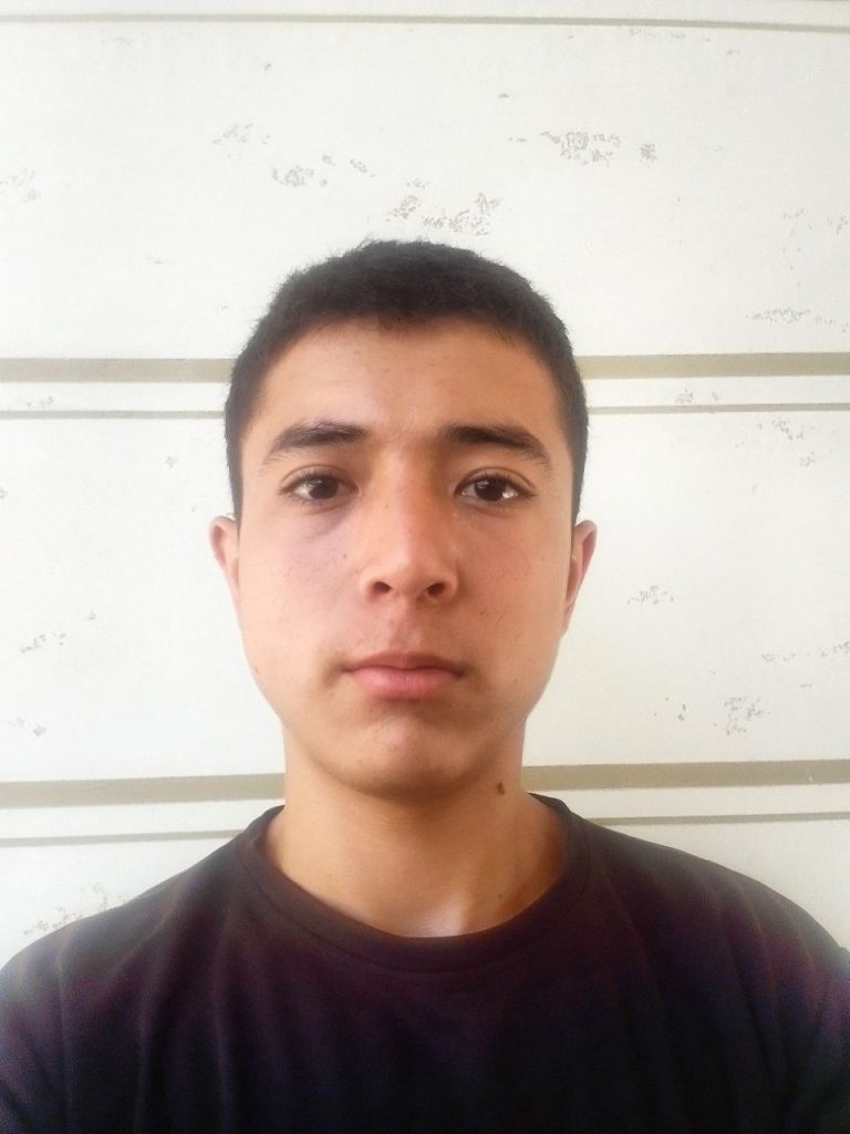 Young Central Asian man with short dark hair, brown eyes, and a black tee shirt. 