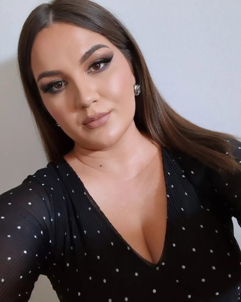 Young Eastern European woman with long dark hair, earrings, and a black top with white dots.