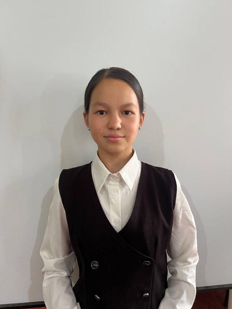 Young Central Asian girl in a black vest over a white top. She has long black hair and brown eyes. 