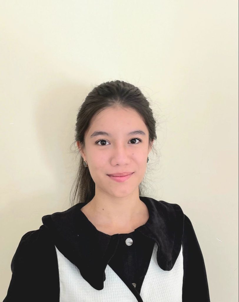 Young Central Asian woman with long dark hair, brown eyes, small earrings, and a black top.