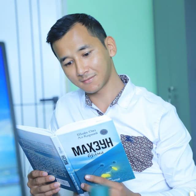 Young Central Asian man in a white collared shirt reading a book.