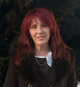 Young middle aged light skinned woman with long curly black hair with red highlights, in a black top.