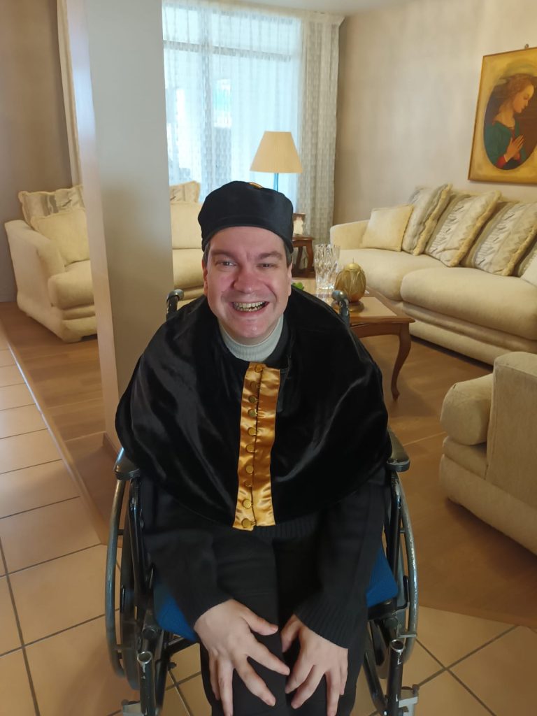 Middle aged Latino man in a jacket, wheel chair and baseball cap in a living room. 