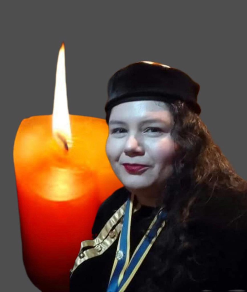 Middle aged Latina woman with dark curly hair and a black beret next to a lighted candle.