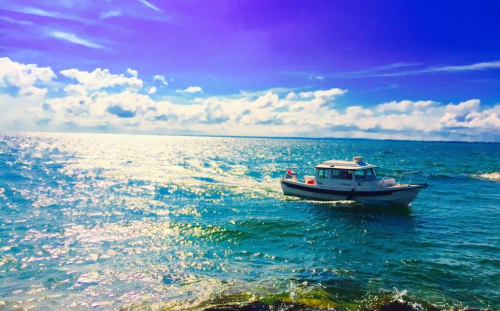 Small boat on blue water near shore, white wispy clouds on a sunny day. 