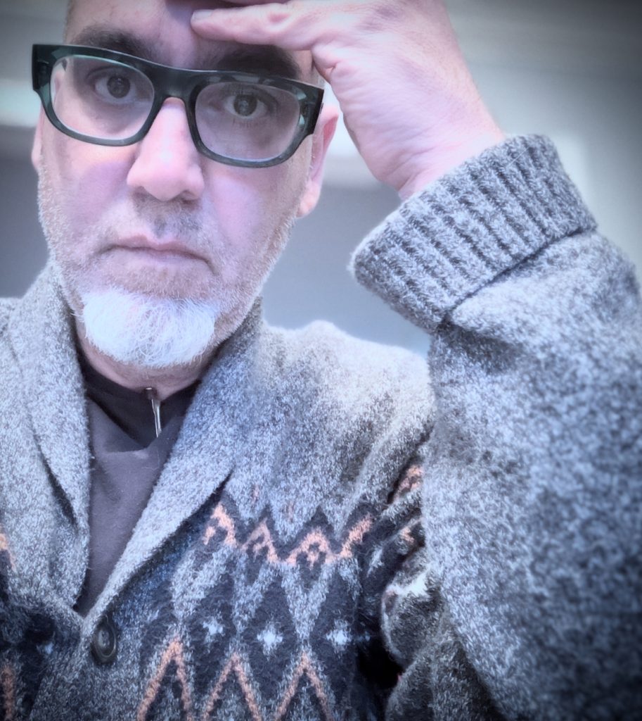 Middle aged white man with glasses and a tan sweater. 