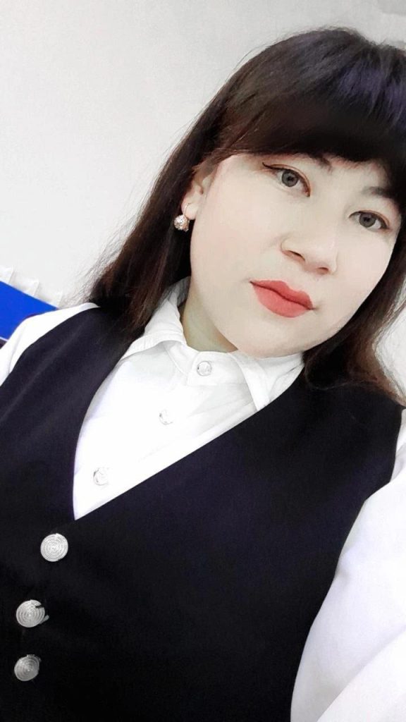 Young Central Asian woman with long dark hair and a white collared shirt and dark vest with white buttons .
