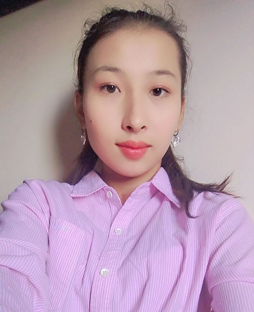 Young Central Asian woman with dark hair and eyes and a pink collared shirt and earrings. 