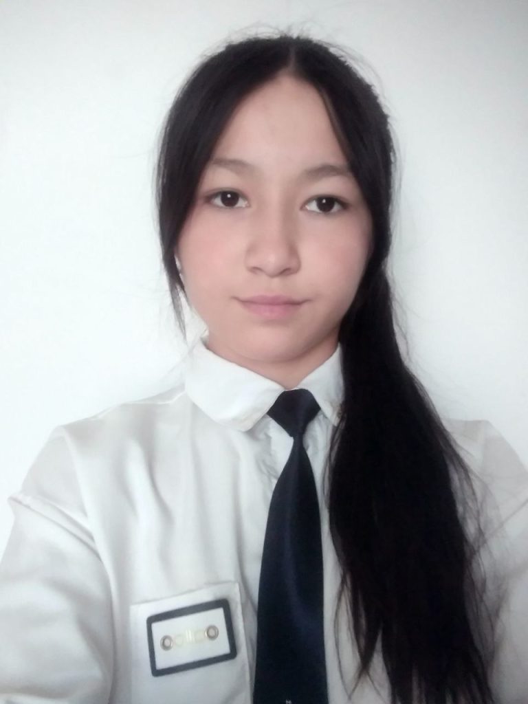 Young Central Asian woman with long straight dark hair and a white top and black tie.