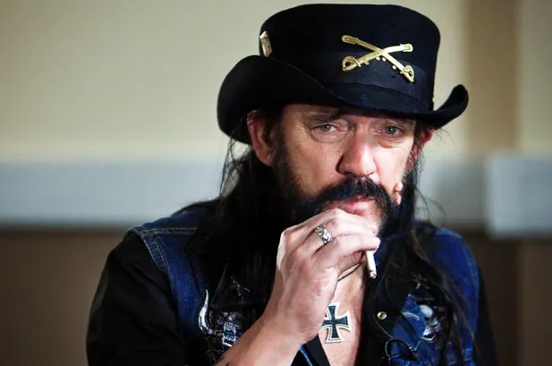 Lemmy from Motorhead. He's middle aged, white, smoking a cigarette, in a jean jacket with long dark hair and a black hat with a design