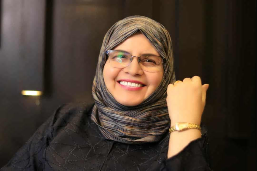 Smiling Middle Eastern woman in a brown patterned headscarf and brown top.