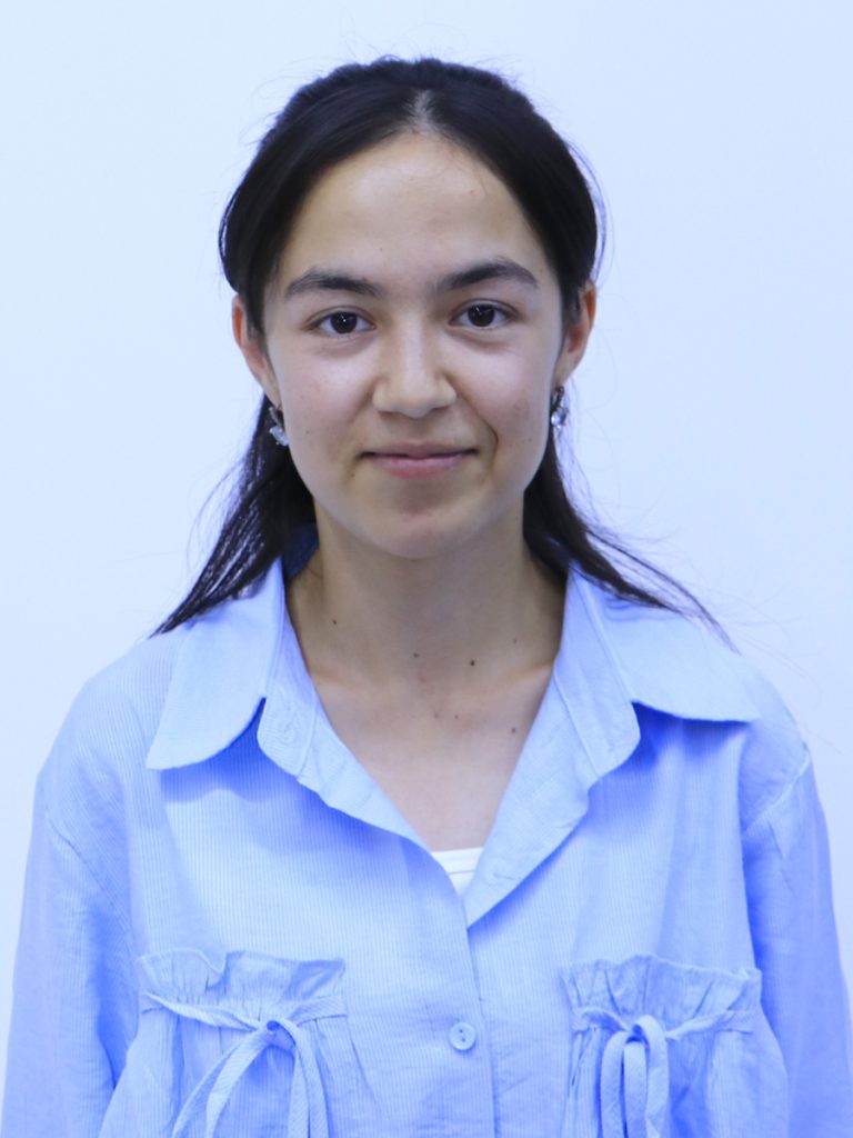 Central Asian young woman with long straight dark hair, brown eyes, small earrings, and a white collared shirt. 