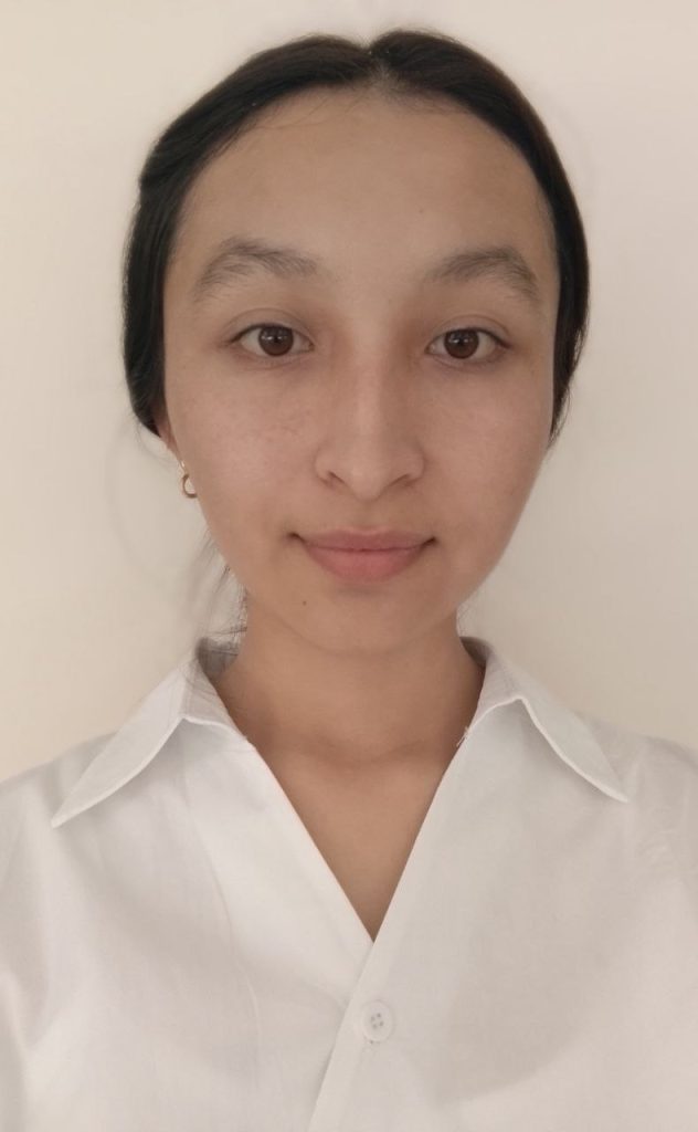 Young Central Asian woman with long dark hair up behind her head, brown eyes, and an earring and a white top. 