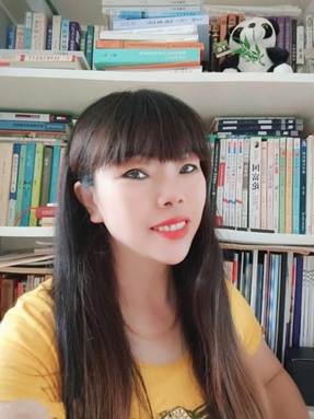 Young East Asian woman with long dark hair, a yellow shirt, and a thin necklace in front of a bookshelf.