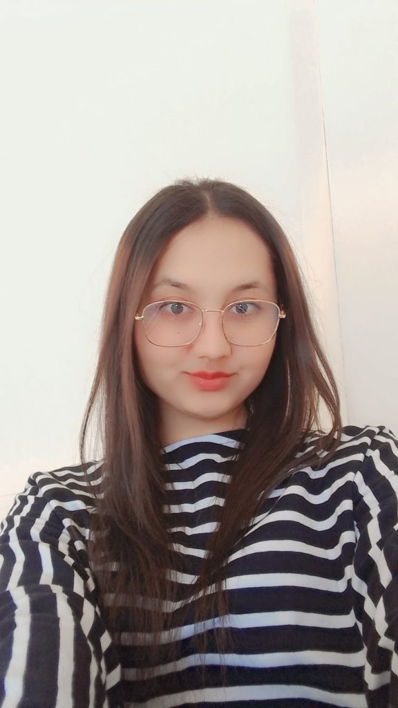Young Central Asian woman with reading glasses, long straight dark hair, and a black and white stripy shirt.