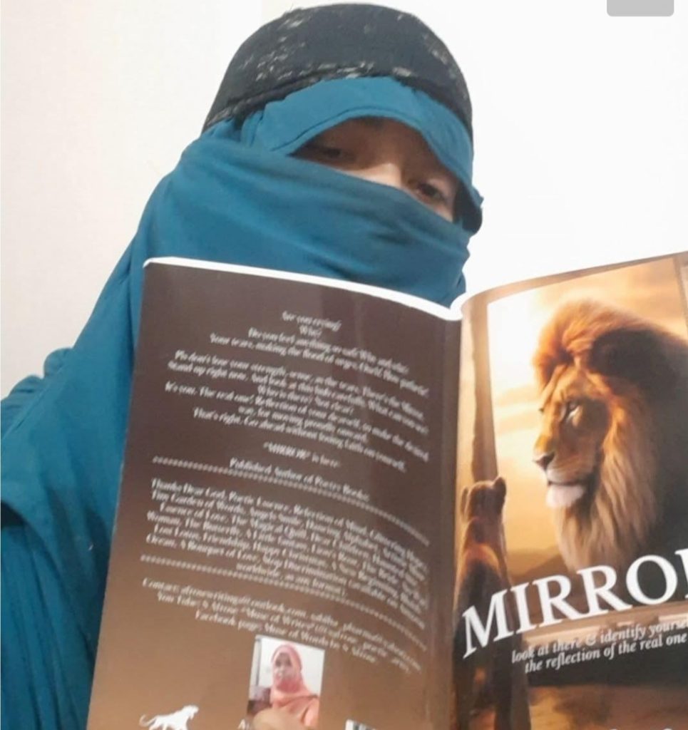 Young Central Asian woman with a blue headscarf that covers her body reading a book with a lion on the front cover. 