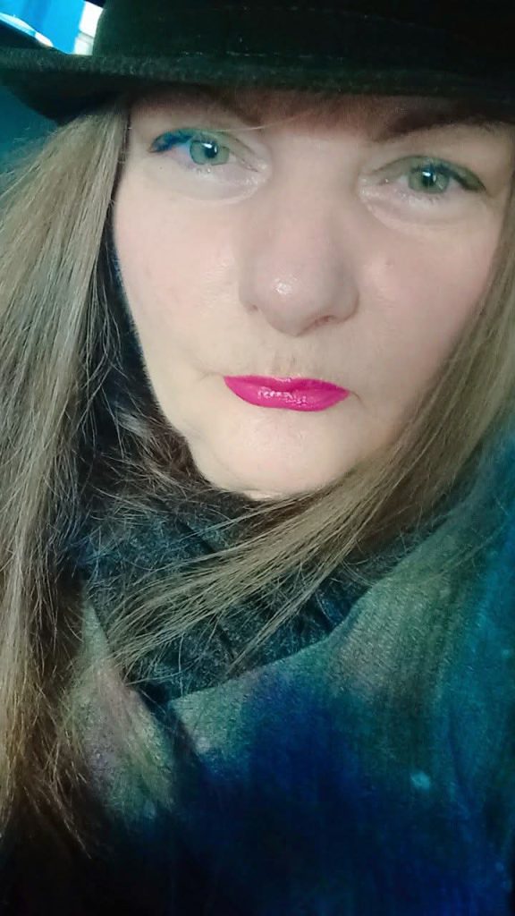 Middle aged European light skinned woman with shoulder length short brown hair, lipstick, and a blue and tan scarf.