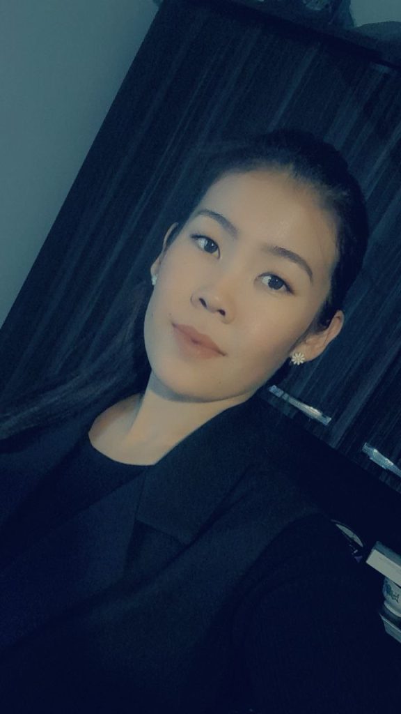 Young Central Asian woman with long dark hair, small earrings, and a black top. 