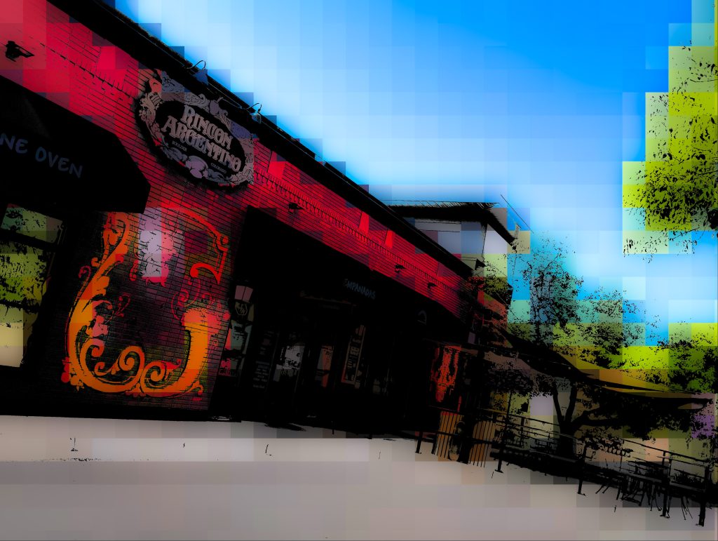 Hazy image of a restaurant with outdoor seating with trees on a sunny day. 