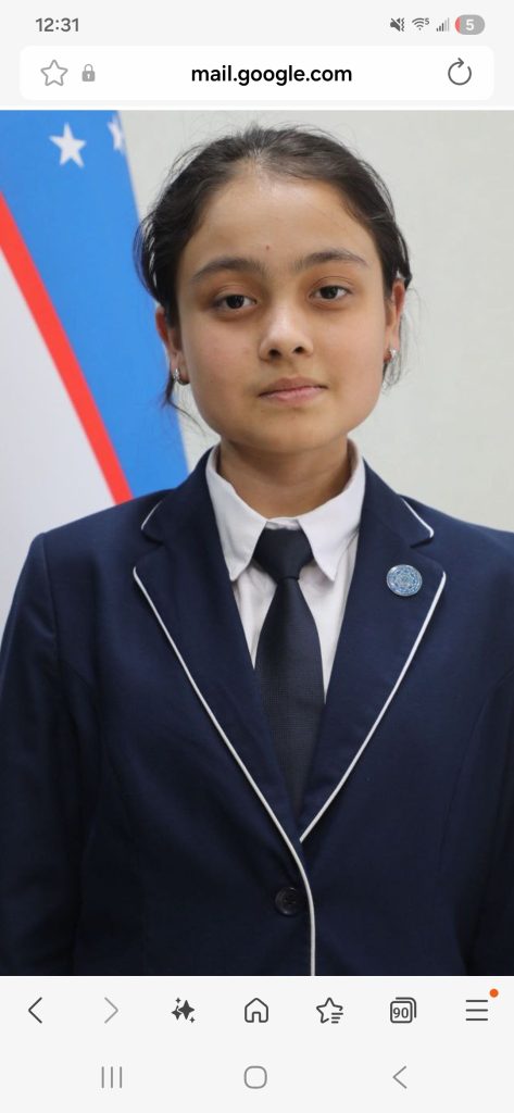 Young Central Asian woman with curly dark hair in a bun, brown eyes, and a blue suit coat and tie. 