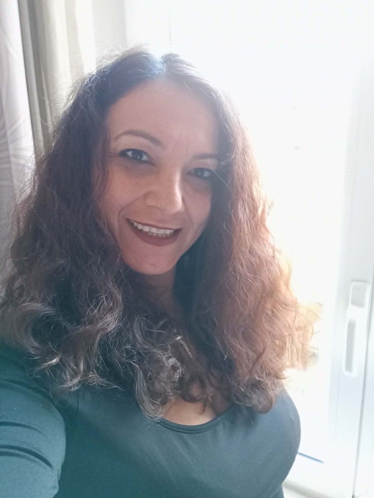 Middle aged smiling Greek woman with shoulder length curly dark hair and a green top.