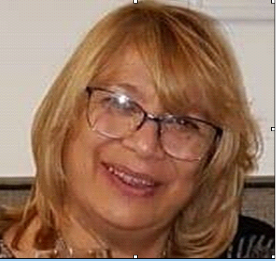 Middle aged woman with short curly blonde hair and reading glasses.
