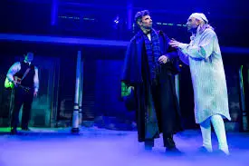 Screen shot of a stage play with an old man in a night cap and white coat talking to a younger man in a suit.