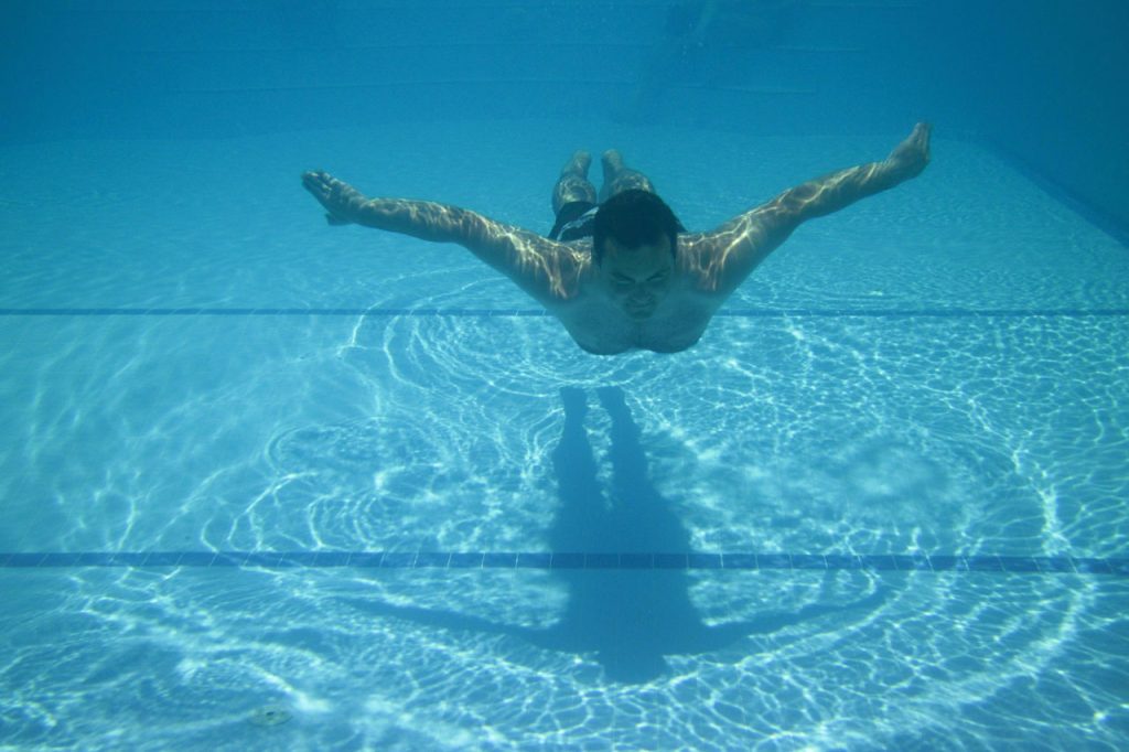 Young light skinned man doing the breaststroke or butterfly stroke in a pool on a sunny day