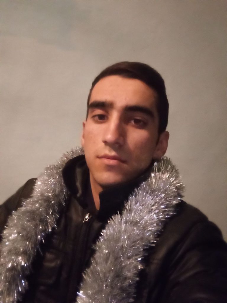 Young adult Central Asian man, short dark hair, clean shaven, dark coat and fluffy gray scarf. 