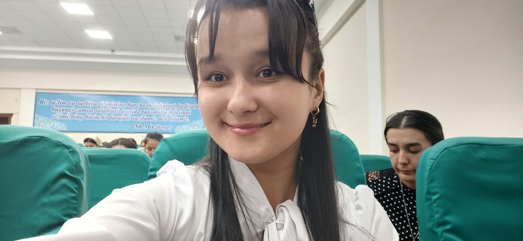 Young Central Asian woman with a white blouse and earrings and long dark hair.
