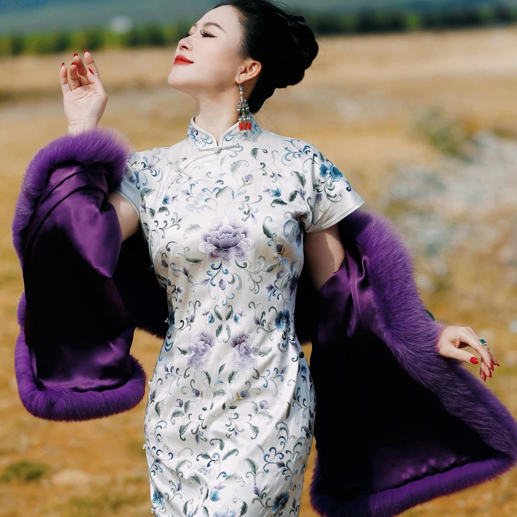 Young East Asian woman with her dark hair up in a bun in a dark purple fur coat over a light silk patterned floral dress.