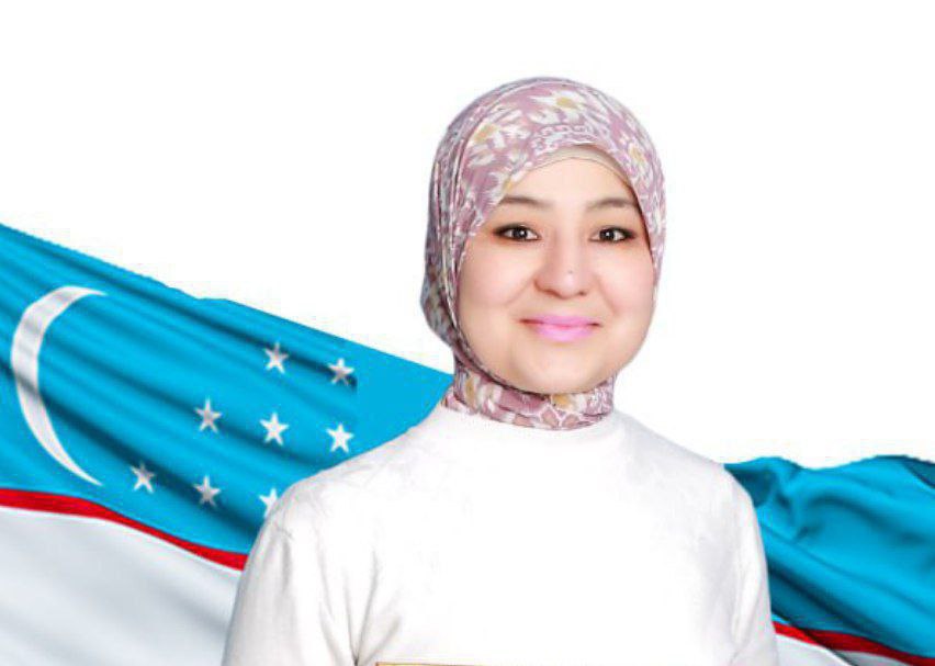 Young Central Asian woman with a pink patterned headscarf and a white top standing in front of a flag.