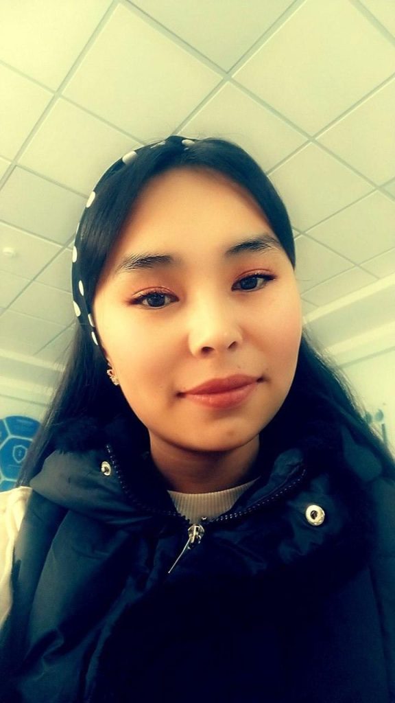 Young Central Asian woman with a black and white spotted headband and black fluffy coat.