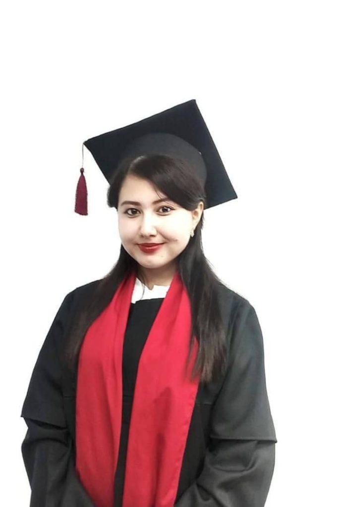 Central Asian woman with long straight dark hair with a black graduation cap and coat and red sash.