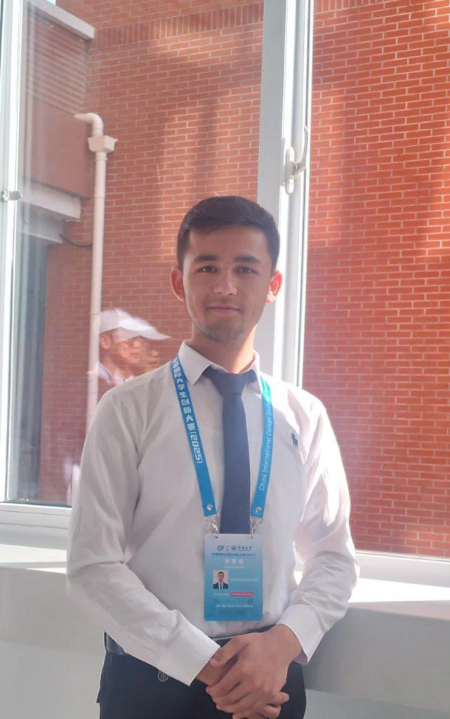 Young Central Asian man standing in front of a brick building in a white collared shirt and black tie. 