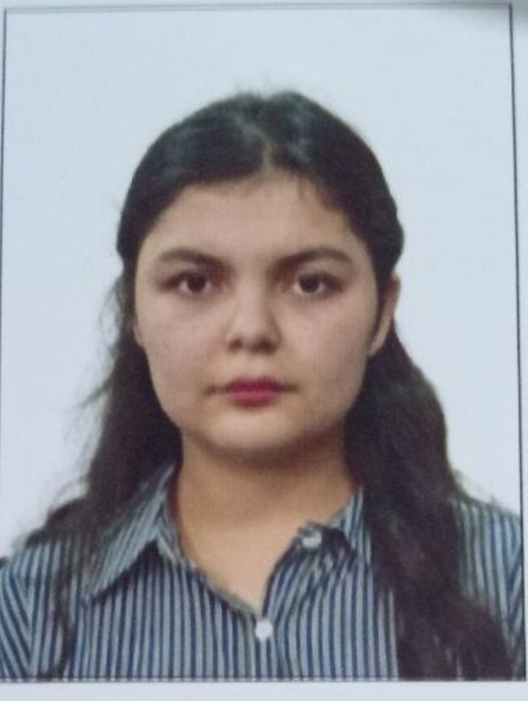 Young Central Asian woman with long dark hair, brown eyes, and a black striped shirt.