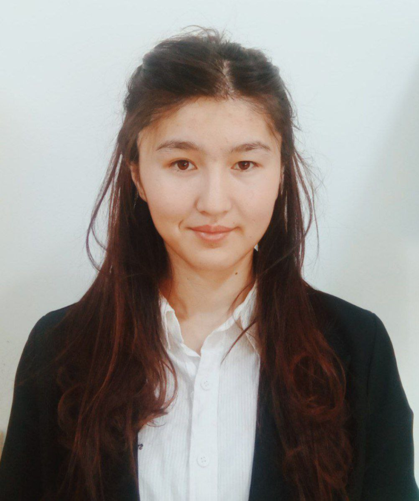 Young Central Asian woman with long dark hair, brown eyes, and a black coat over a white collared shirt.
