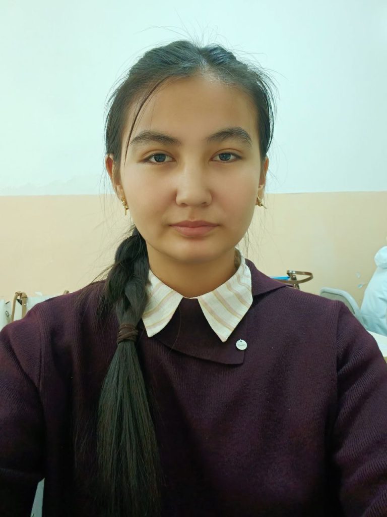 Young Central Asian woman with long dark hair in a ponytail and a purple sweater.