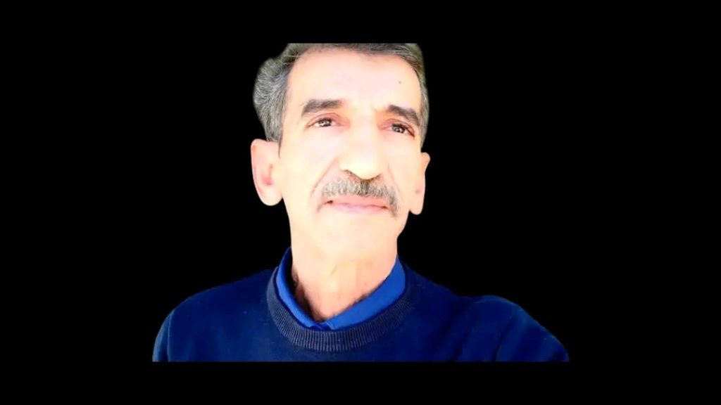 Middle aged Egyptian man with salt and pepper hair and a blue sweater. 