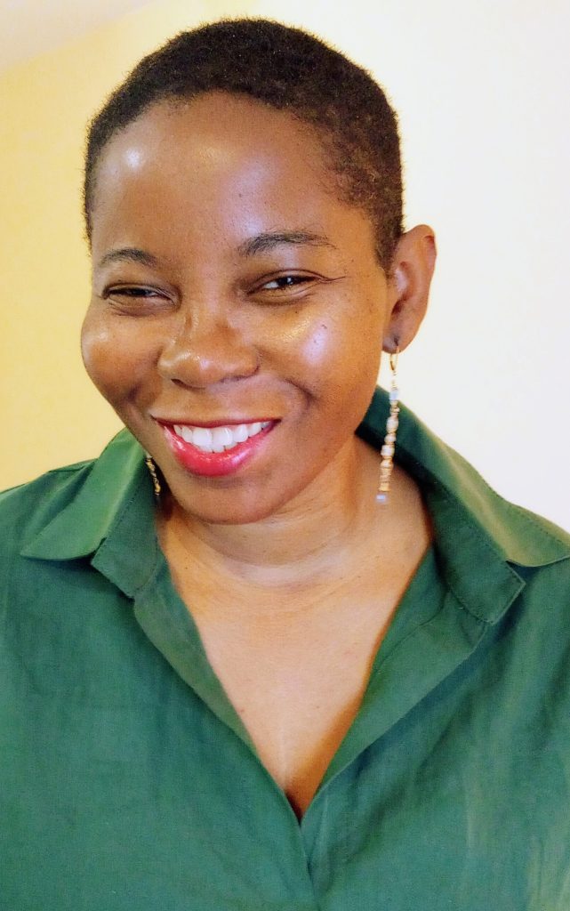 Smiling young middle aged Black woman with long white earrings and a green top. 