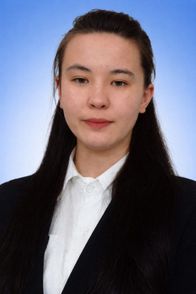 (Young Central Asian woman with long dark hair and a black coat over a white collared top)