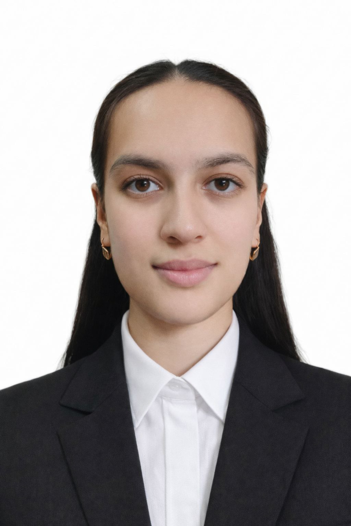 Young Central Asian woman with brown eyes, long straight brown hair, small earrings, and a black coat over a white collared top.