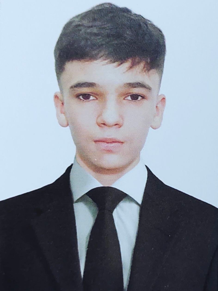 Young Central Asian man with short brown hair, brown eyes, and a black suit and tie. 